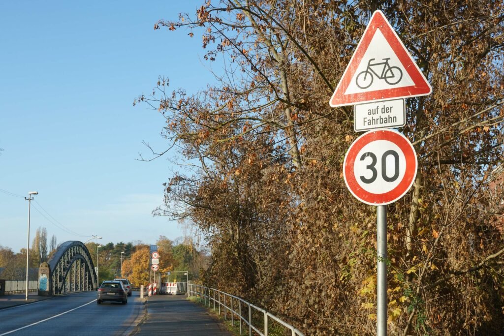Schild Gefahrenzeichen „Achtung Radfahrer" kombiniert mit Schild Geschwindigkeitsbegrenzung 30 an der Auffahrt zur Brücke.