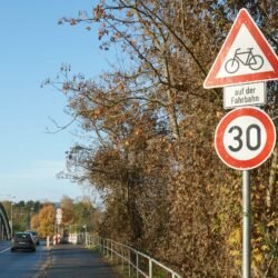 Schild Gefahrenzeichen „Achtung Radfahrer" kombiniert mit Schild Geschwindigkeitsbegrenzung 30 an der Auffahrt zur Brücke.