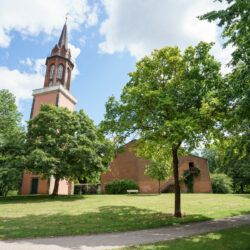 Eine Kirche mit separat stehendem Turm. Davor eine Wiese mit Bäumen